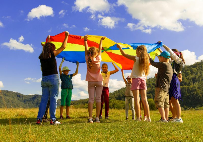 Kids playing with a rainbow parachute on a sunny day